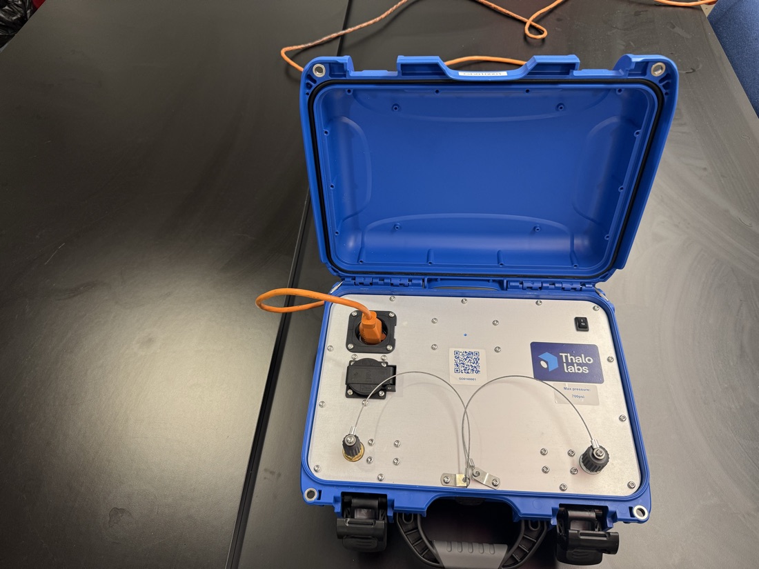 Gordon's blue case open on a table: orange power cord plugged into the top-left socket, rocker switch at top right, and the two capped front ports at the bottom of the panel