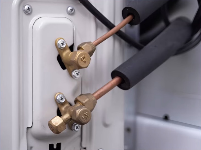 The two brass service valves on the side of the outdoor unit: the small liquid line above and the larger insulated suction line below